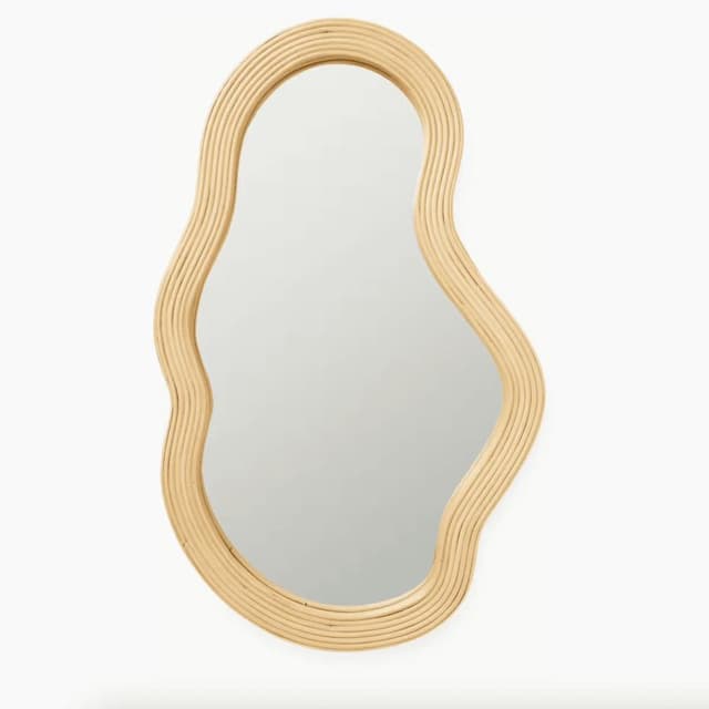 Un miroir asymétrique de forme organique avec un cadre ondulé en bois clair sur fond blanc.