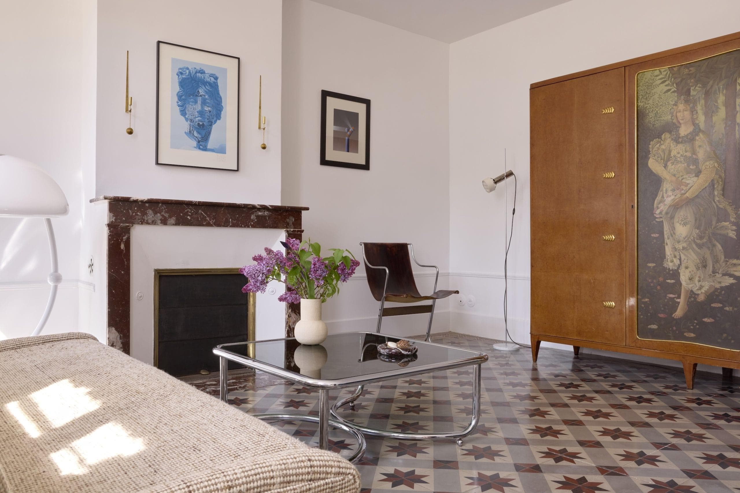 Un salon élégant avec un canapé moderne et une table basse en verre sur un sol à motifs. Les objets décoratifs comprennent un vase avec des fleurs, des œuvres d'art murales et une armoire en bois vintage. Un lampadaire est placé dans le coin à côté d'une chaise du milieu du siècle.