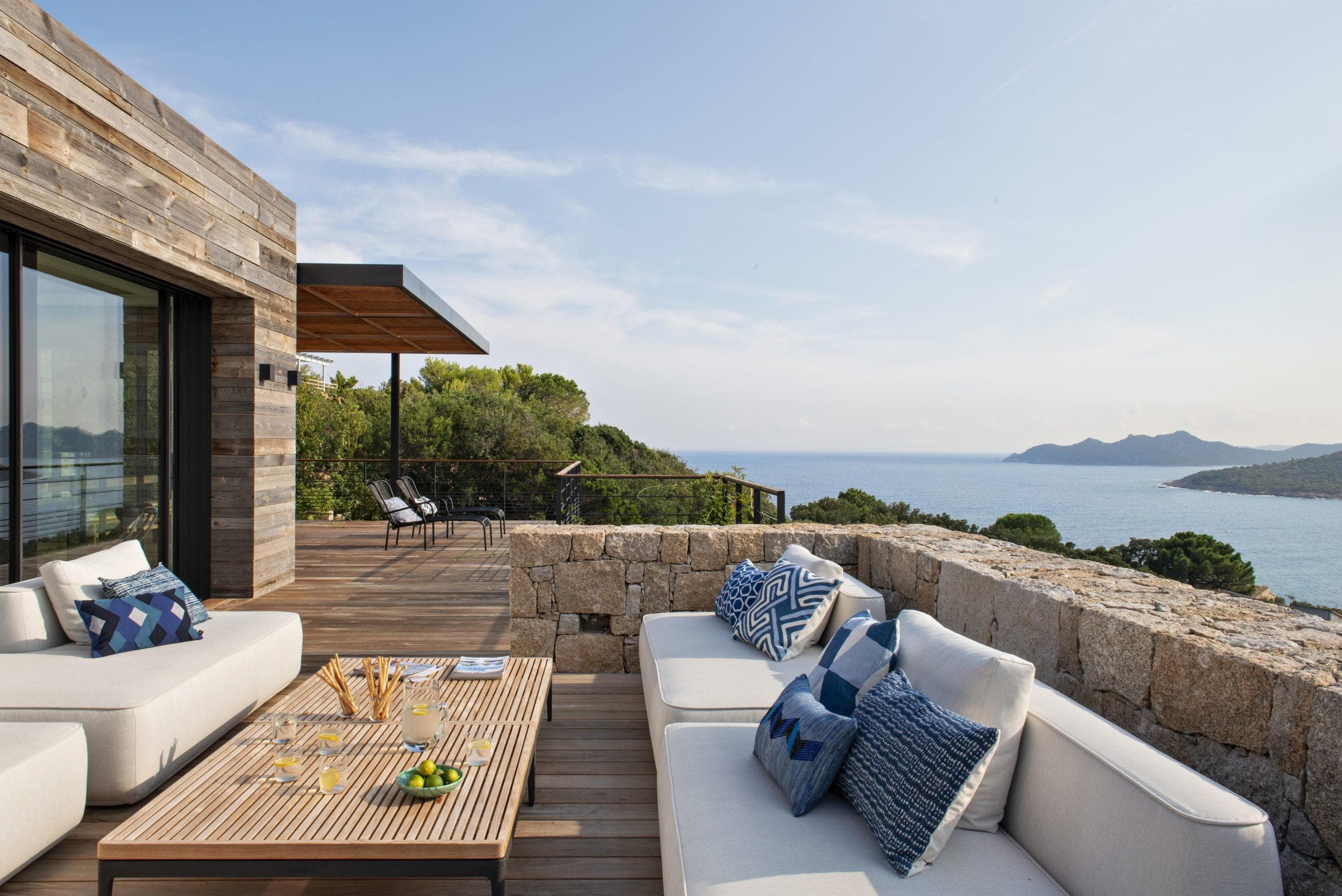 terrasse en bois avec rambarde en pierre, les canapés de la villa disposent d'une vue sur la mer