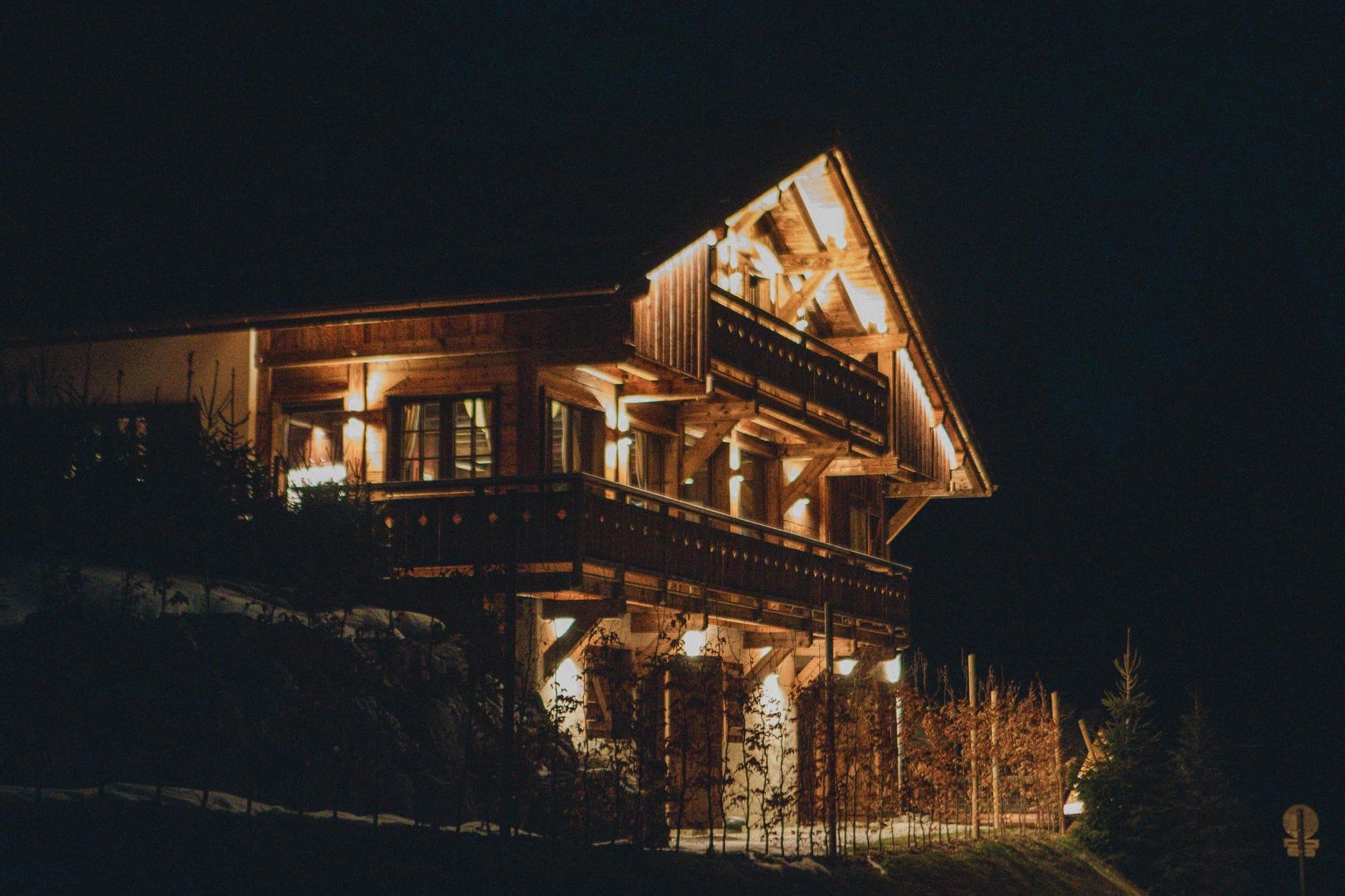 Under the stars, Chalet Domino Quatre lights up, showcasing its wooden facade and warm ambiance in the heart of the snow-covered mountains.