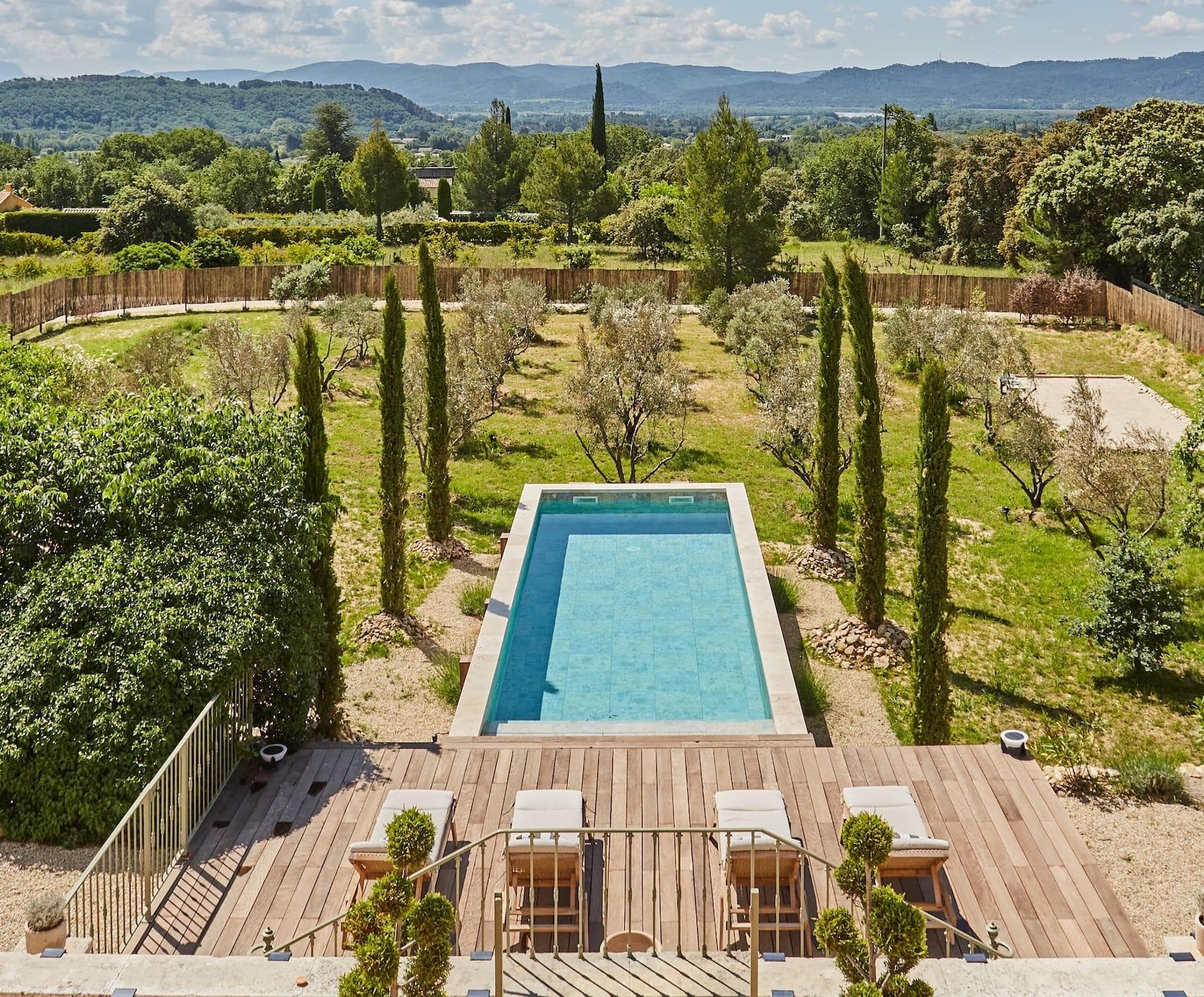 Panoramic views from the terrace overlooking a swimming pool, cypress trees and mountains in the distance.